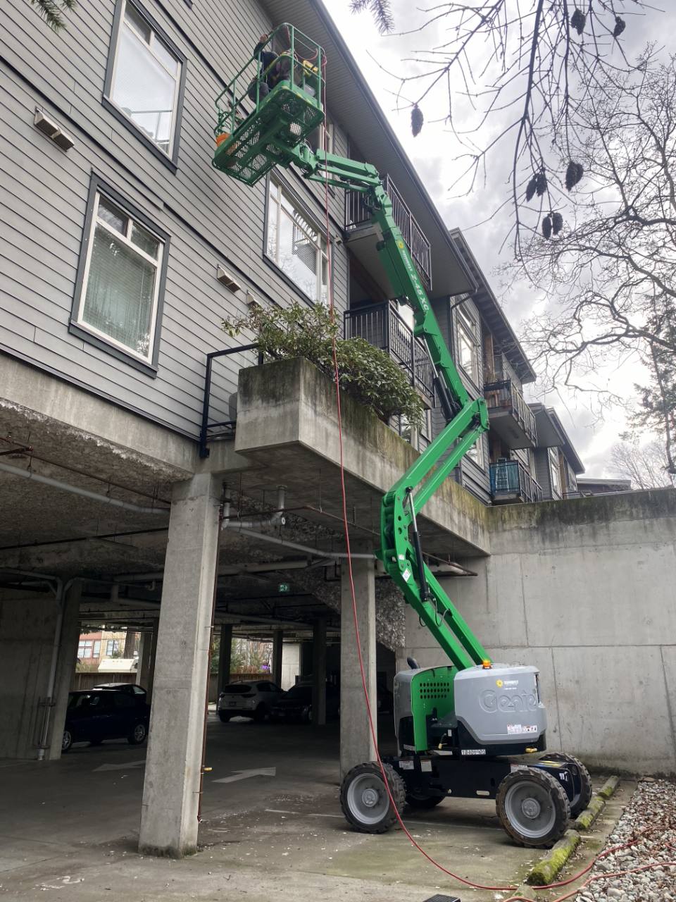 Employee working from a green articulated boom lift beside an apartment building