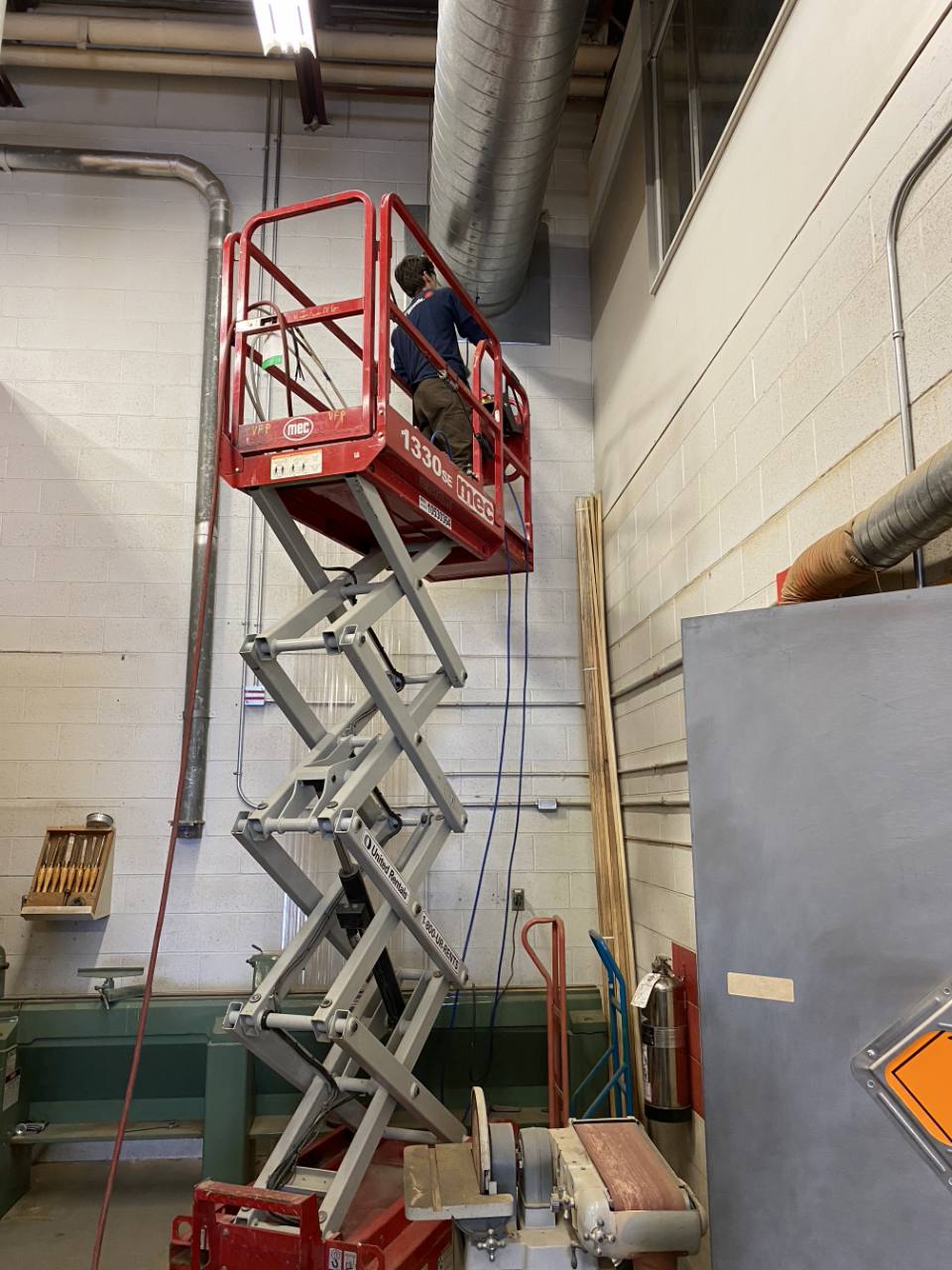 Employee using an indoor scissor lift to access commercial ductwork