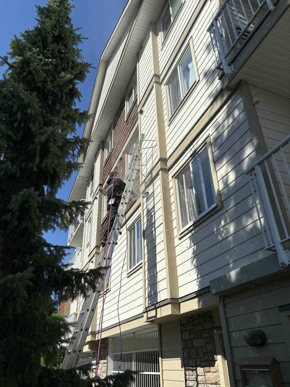 Employee performing exterior service from a ladder on a multi-storey building